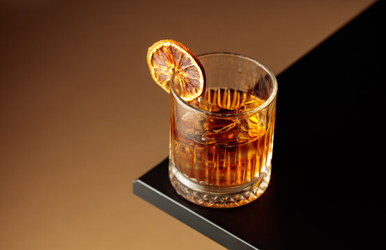Old-fashioned cocktail with ice and a dried orange slice.