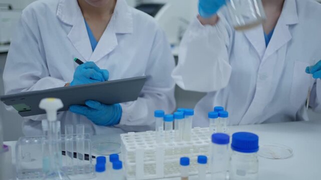 Scientists working together in a laboratory analyzing samples and recording experiment data on a tablet
