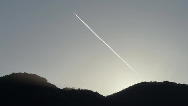 Contrail of an airplane flying over mountains at sunrise