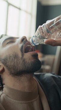 Vertical shot of young adult Middle Eastern man drinking water from plastic bottle during volunteer work break. Footage is ideal for humanitarian aid campaigns and non-profit organization promos