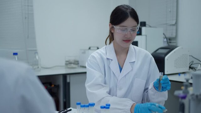 Asian female scientist pouring liquid from a beaker into a test tube during a laboratory experiment for research and development