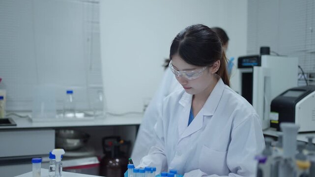 Female scientist conducting research experiment and analyzing sample in a modern science laboratory with a colleague in background
