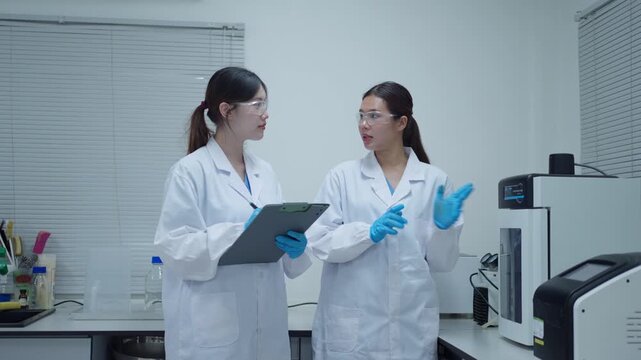Two female scientists collaborating on research and discussing experiment results in a modern laboratory