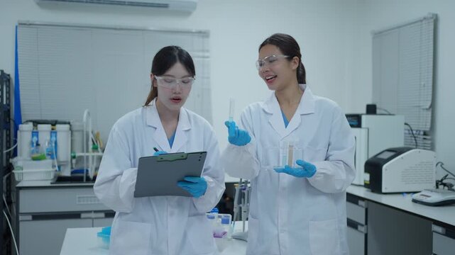 Two female scientists discussing experiment results while holding a test tube and clipboard in a modern laboratory