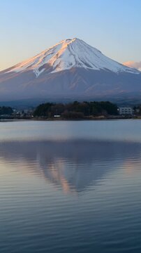 早朝の柔らかな光に照らされた雪化粧の雄大な富士山が静寂な湖面に完璧にその姿を映し出す、息をのむような日本の冬景色