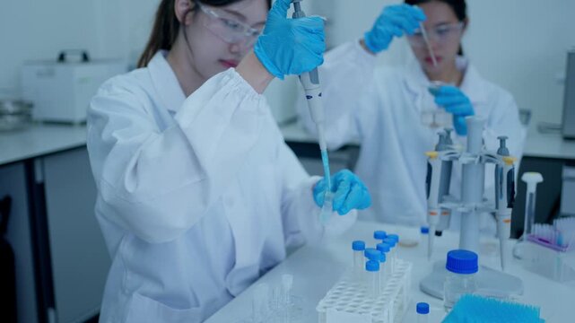 Two female scientists working with pipettes and test tubes in a modern research medical laboratory for vaccine development