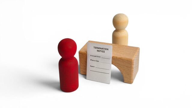 Close-up view of employment termination notice and wooden peg dolls representing a corporate layoff concept.
