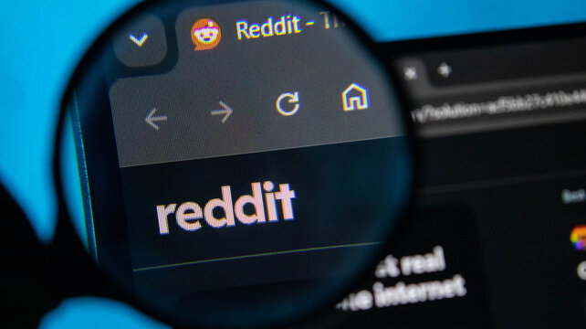 Magnifying glass focused on Reddit website interface on a dark screen with blue reflections