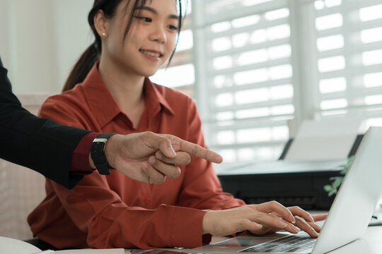 Business Manager Points at Laptop Screen, Guiding Female Colleague at Desk