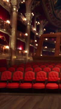 Rows of red chairs sit empty in a theater waiting for guests. The stage area is dark, with lights creating a slight glow. The atmosphere is filled with anticipation for the show.