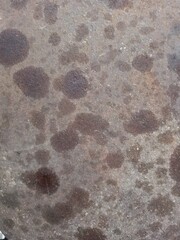 Concrete surface displays dark circular stains creating a weathered and industrial aesthetic with a rough and gritty texture. © Mari Lim
