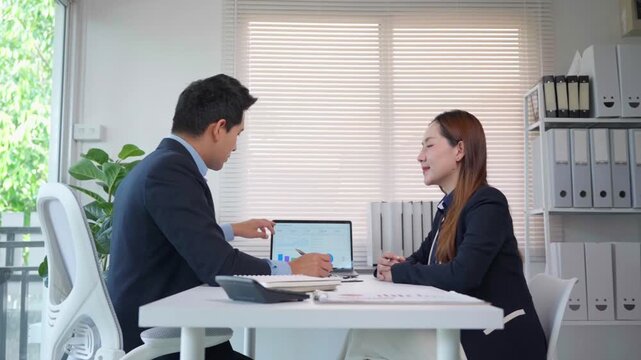 Asian business colleagues discussing a project and analyzing financial data on a laptop during a meeting in a modern office