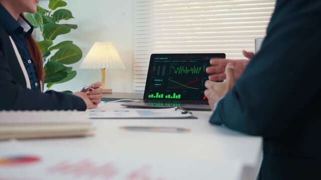 Financial analysts discussing stock market trading charts on a laptop in a modern office meeting