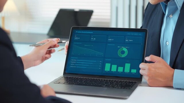 Business colleagues analyzing carbon neutral dashboard data on a laptop for ESG and net zero emission strategy in a modern office