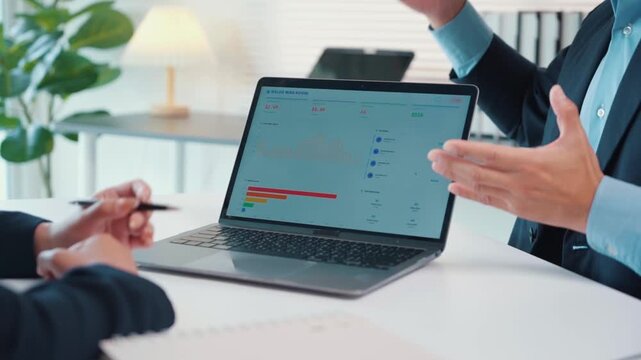 Business colleagues reviewing sales data and analytics on a laptop screen during a corporate office meeting