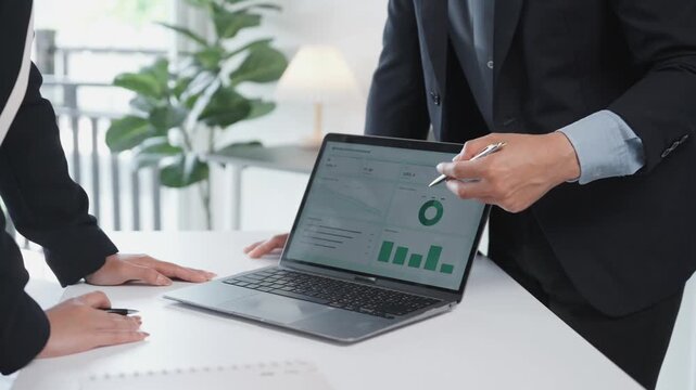Business colleagues analyzing financial data charts and sales performance on a laptop screen during an office meeting