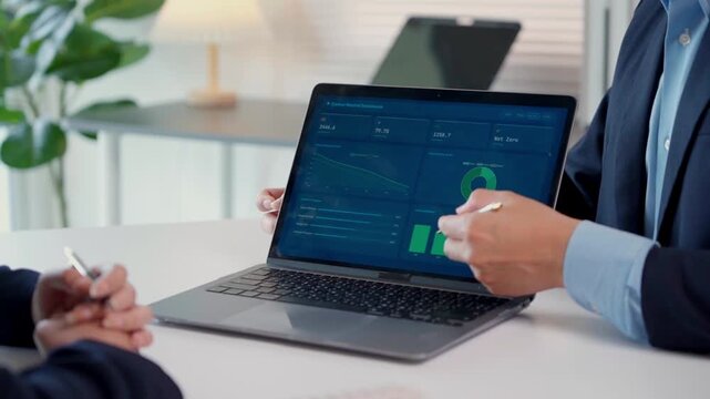 Businessman presenting financial data analytics on a laptop screen during a corporate meeting with a client in a modern office