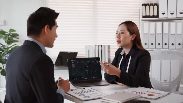 Financial advisor presenting investment strategy and stock market data on laptop to a business client in a modern office meeting