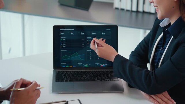 Businesswoman analyzing supply chain data on a laptop dashboard during a corporate meeting with a colleague in the office