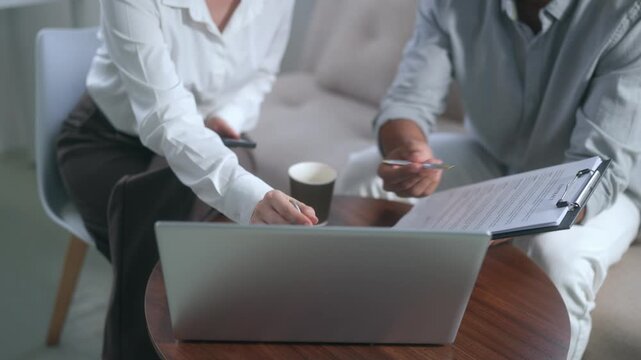 Business colleagues reviewing contract terms and using smartphone calculator for financial analysis in modern office meeting