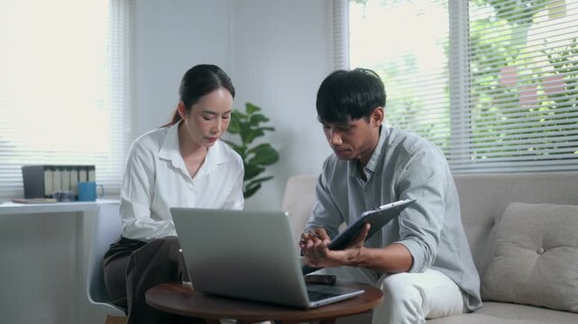 Asian colleagues collaborating on project and discussing business strategy in a modern office with a laptop and documents