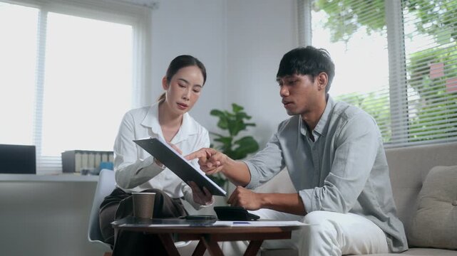 Financial advisor discussing investment plan with a male client using a clipboard and calculator in a modern office living room
