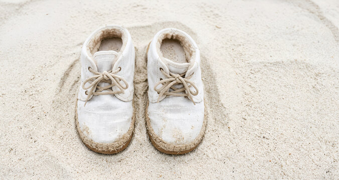 Immagine con primo piano di un vecchio paio di scarpe in tela bianca lasciate su una superficie di fine sabbia bianca