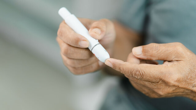 Close-up of a senior adult using a lancet device for finger prick blood glucose testing at home. Diabetes self-monitoring promotes preventive healthcare, chronic disease management.