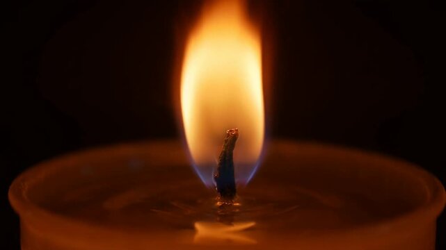 Close-up of a burning candle wick with a glowing warm flame in the dark
