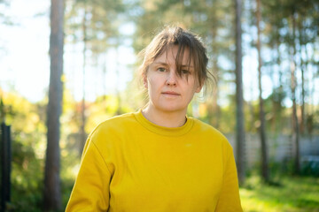 Fototapeta premium A woman in a yellow shirt looks at the camera with a relaxed, confident expression in a field. The calm farmer gazing ahead presents a grounded, natural moment on agricultural land.