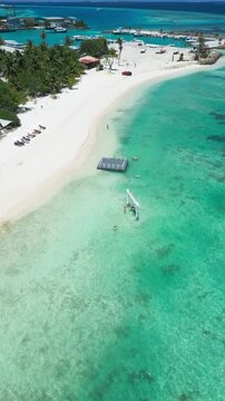 Aerial village harbor and sandy beach, small marina and palmfringed village, docks and moored boats in shallow turquoise water, local coastal activity and resort amenities, Himmafushi, Maldives