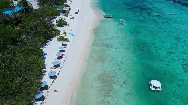 Aerial floating dome near shoreline, white dome in shallow turquoise water, lined umbrellas and sunbeds on white sand, palm fringe and resort vibe, drone hospitality shot,