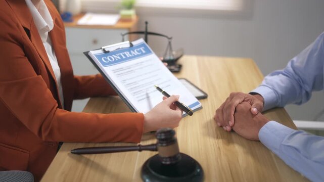 Female lawyer explaining a contract to a male client with a gavel and scales of justice on the office desk