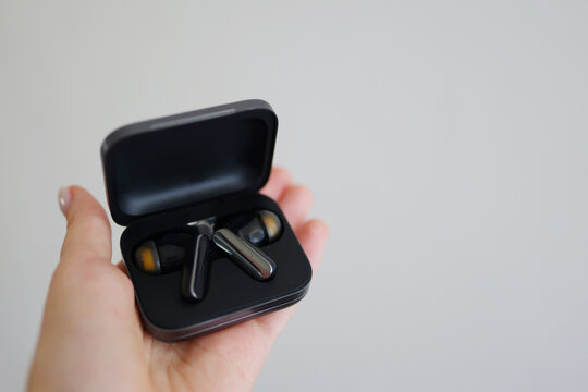 Close-up of true wireless earbuds in an open charging case held in hand against a clean background with copy space.