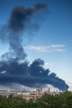 Major fire at production facility with thick dark smoke rising from industrial area over city, oil refinery plant disaster, increased fire complexity, release of harmful substances into air.