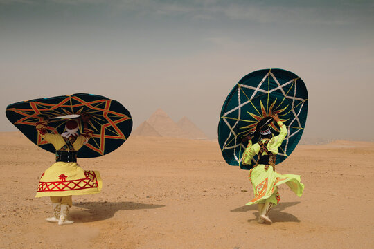 Two tanoura dance performers in vibrant neon folk costumes spin ornate disc props at Giza Pyramids Egypt desert ideal for cultural tourism