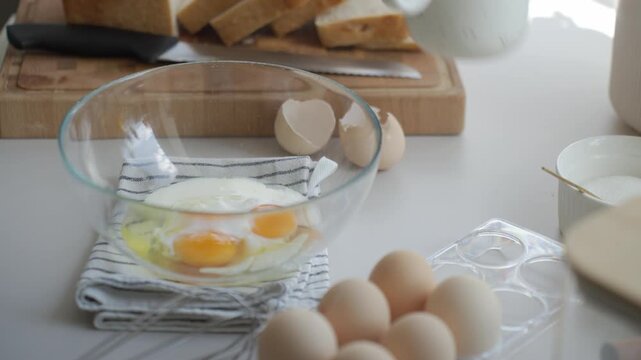 Hand adds milk and sugar to eggs in bowl with sliced bread nearby