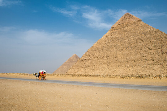 Traditional horse carriage in motion along a desert road beside the massive Giza Pyramids under a clear blue sky highlighting ancient Egypt travel