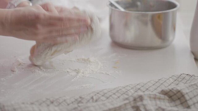 Hands knead dough on floured counter, with saucepan and checked towel nearby
