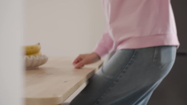 Woman sitting at table, pulling out a gray chair beside a wooden tabletop