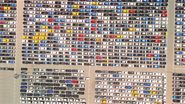 A drone descends toward a massive terminal packed with thousands of neatly parked cars