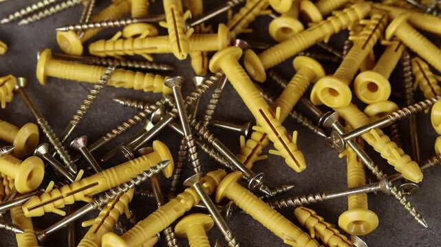 Yellow plastic dowels with metal screws fall on a gray surface. Top view of scattered construction fasteners. Dowel with a screw for quick installation. Close-up of fasteners for construction work