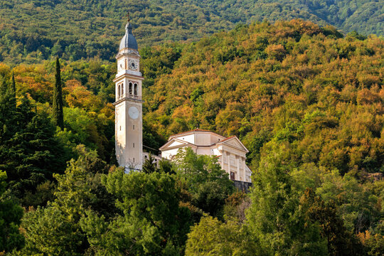Sanctuary of Saint Orso in Santorso, Italy, stands among lush green trees and forested hills, with its historic bell tower creating a scenic summer landscape.