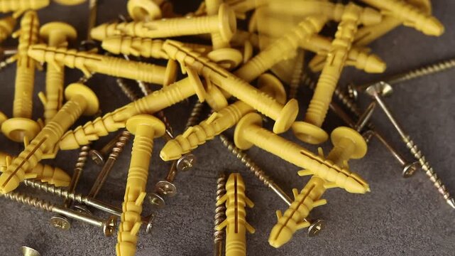 Yellow plastic dowels with metal screws fall on a gray surface. Top view of scattered construction fasteners. Dowel with a screw for quick installation. Close-up of fasteners for construction work