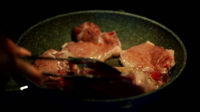 Chef Hand Using Tongs To Flip Raw Meat Steaks In Hot Frying Pan. Cooking Pork Chops