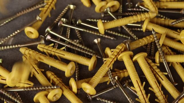 Yellow plastic dowels with metal screws fall on a gray surface. Top view of scattered construction fasteners. Dowel with a screw for quick installation. Close-up of fasteners for construction work