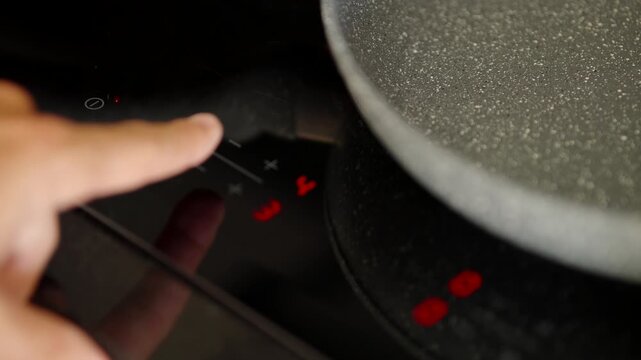 Person Hand Pressing Button On Modern Induction Cooktop Controlling Temperature. Electric Stove Smart Touch 