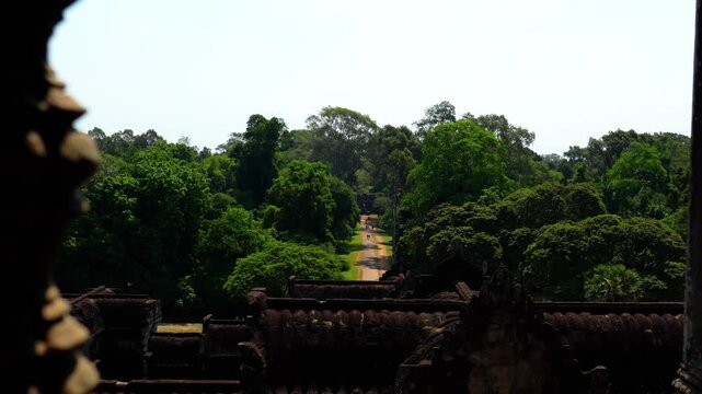 Scenic view from inside the ancient Angkor Wat temple overlooking a lush tropical forest and historic pathway in Siem Reap, Cambodia. Cinematic footage capturing the iconic Khmer temple architecture