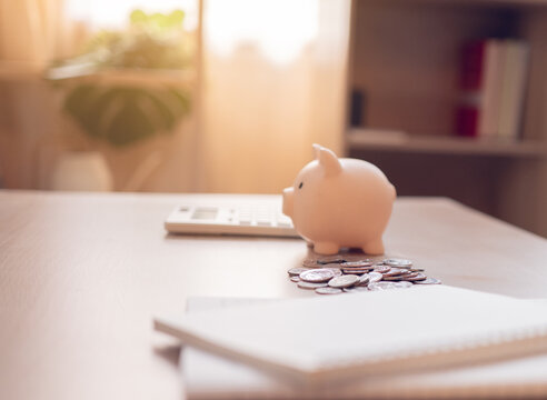 PInk piggy bank with coins beside a calculator on a home desk, symbolizing budgeting and smart saving