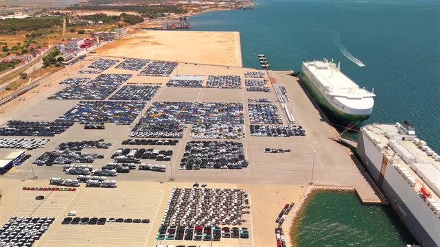 Thousands of cars sit parked at a vehicle export terminal beside a car carrier ship